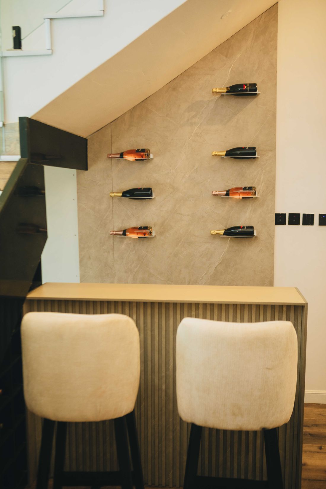 A bar counter with high stools set beneath the staircase, bottles displayed on the wall